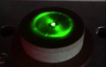 First close-up of a circular Ferrocell glowing green above a magnet.