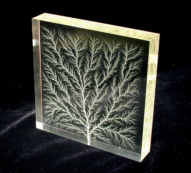 Transparent acrylic block containing a white branching Lichtenberg discharge pattern.