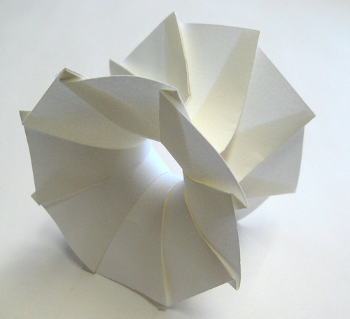 White folded-paper sculpture forming a twisted ring around a central opening.