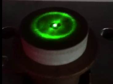 Second close-up of a circular Ferrocell glowing green above a magnet.